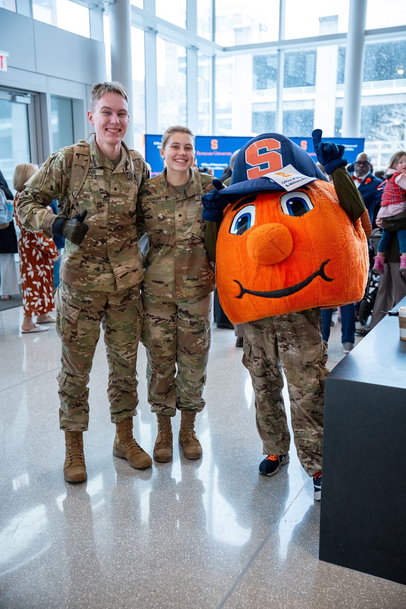 two people in uniforms standing with Otto the Orange inside a building with expansive windows