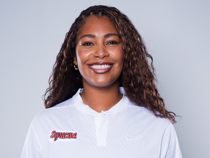 Person wearing a white collared athletic shirt with the word “Syracuse” in red script and a Nike logo on the chest