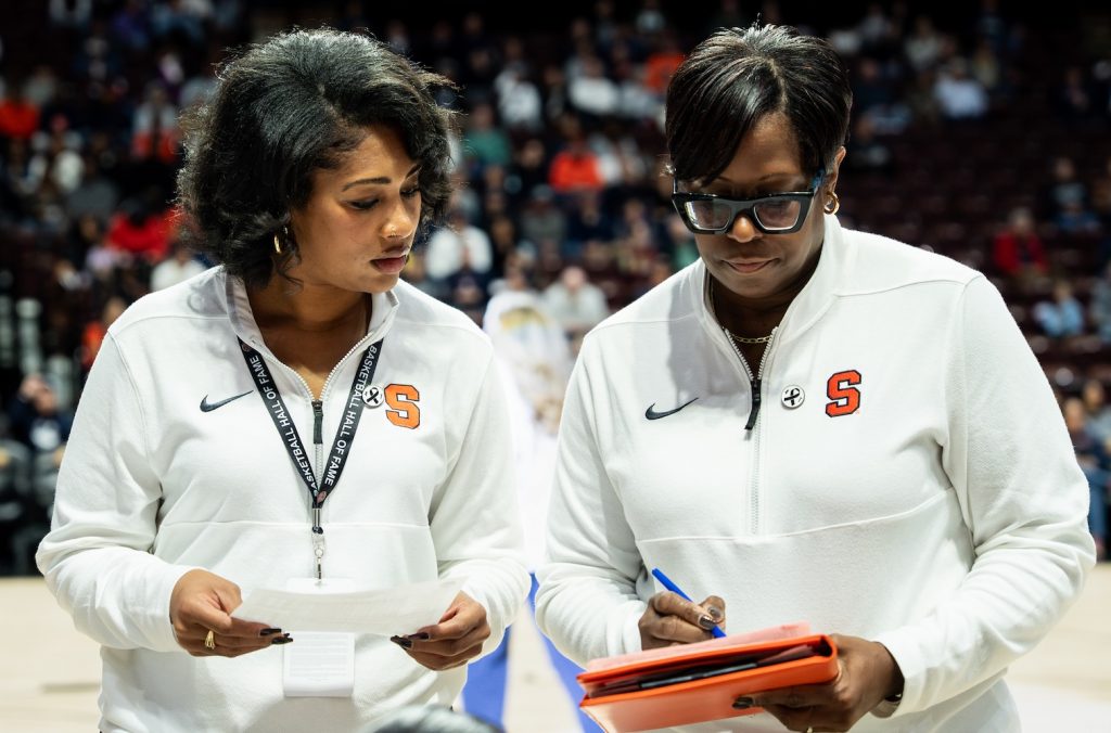 Two individuals, holding papers and a clipboard, standing courtside