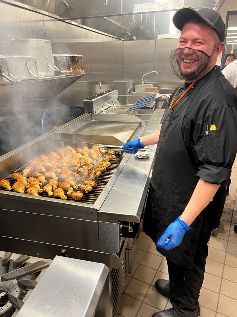 A chef grills chicken on a flatop in the athletic dining kitchen.