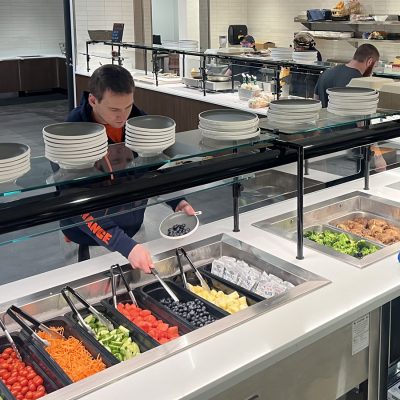 A student-athlete selects fresh fruit and vegetables from the salad bar at the OneTeam Dining Center in Syracuse University's John A. Lally Athletics Complex.