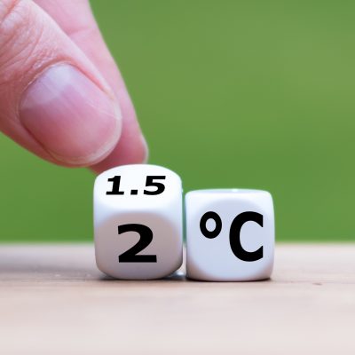 Symbol for limiting global warming. Hand turns a dice and changes the expression "2°C" to "1.5°C", or vice versa.