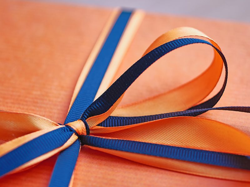 An orange gift wrapped with an orange and blue bow