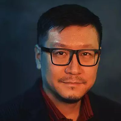 Man with dark hair and glasses and moustache, smiling