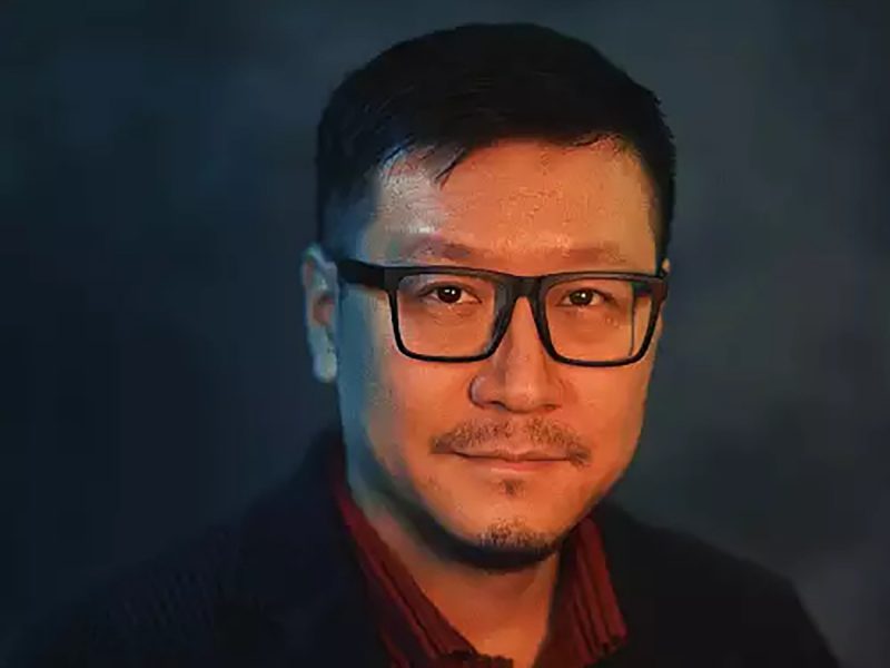 Man with dark hair and glasses and moustache, smiling