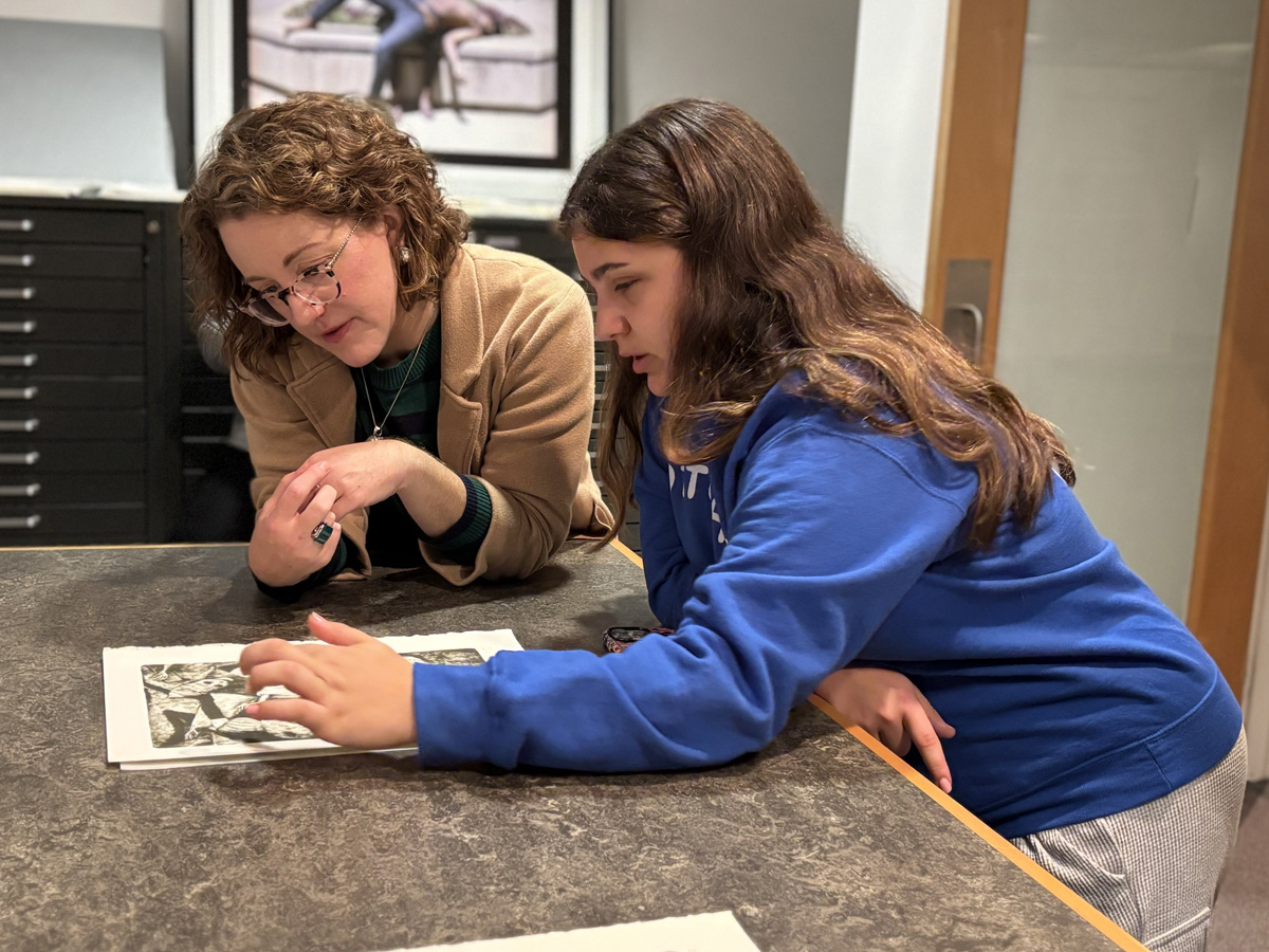 Two people leaning over a table in an art study room, closely examining a black-and-white print and discussing its details