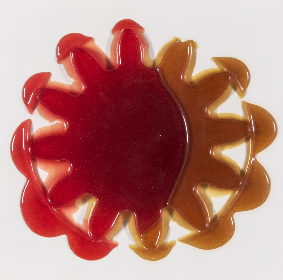 Glossy, gear-like shape in red and brown hues on a white background, resembling a stylized sunburst or abstract form