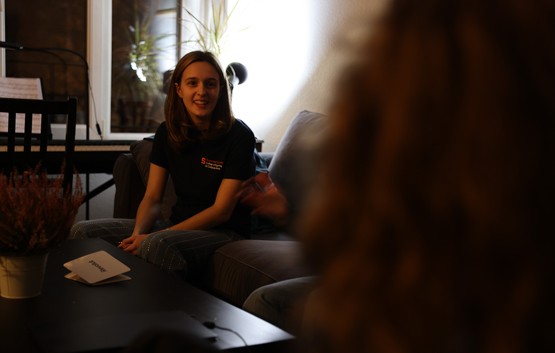 Person sitting on a couch in a living room with a piano in the background, a coffee table with a plant and papers in the foreground