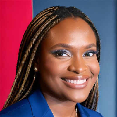 Professional headshot of a smiling person wearing a blue blazer against a red and blue background.