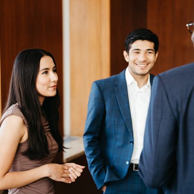 Three professionals engaged in conversation in a modern office setting with wood-paneled walls