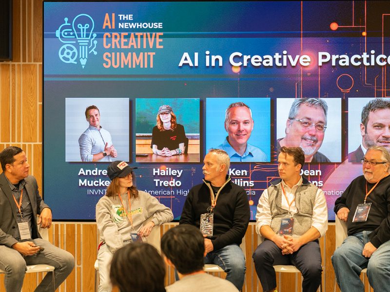 Panel discussion at the Newhouse AI Creative Summit with five speakers seated on stage in front of a large screen displaying the event title 'AI in Creative Practice' and speaker names. Audience members are visible in the foreground