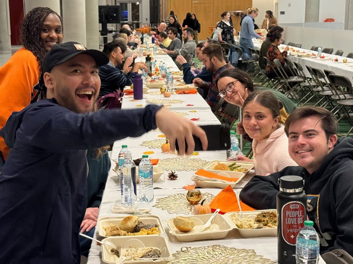 Long table set for a Friendsgiving meal with trays of food, water bottles, and festive decorations, as people sit and take photos