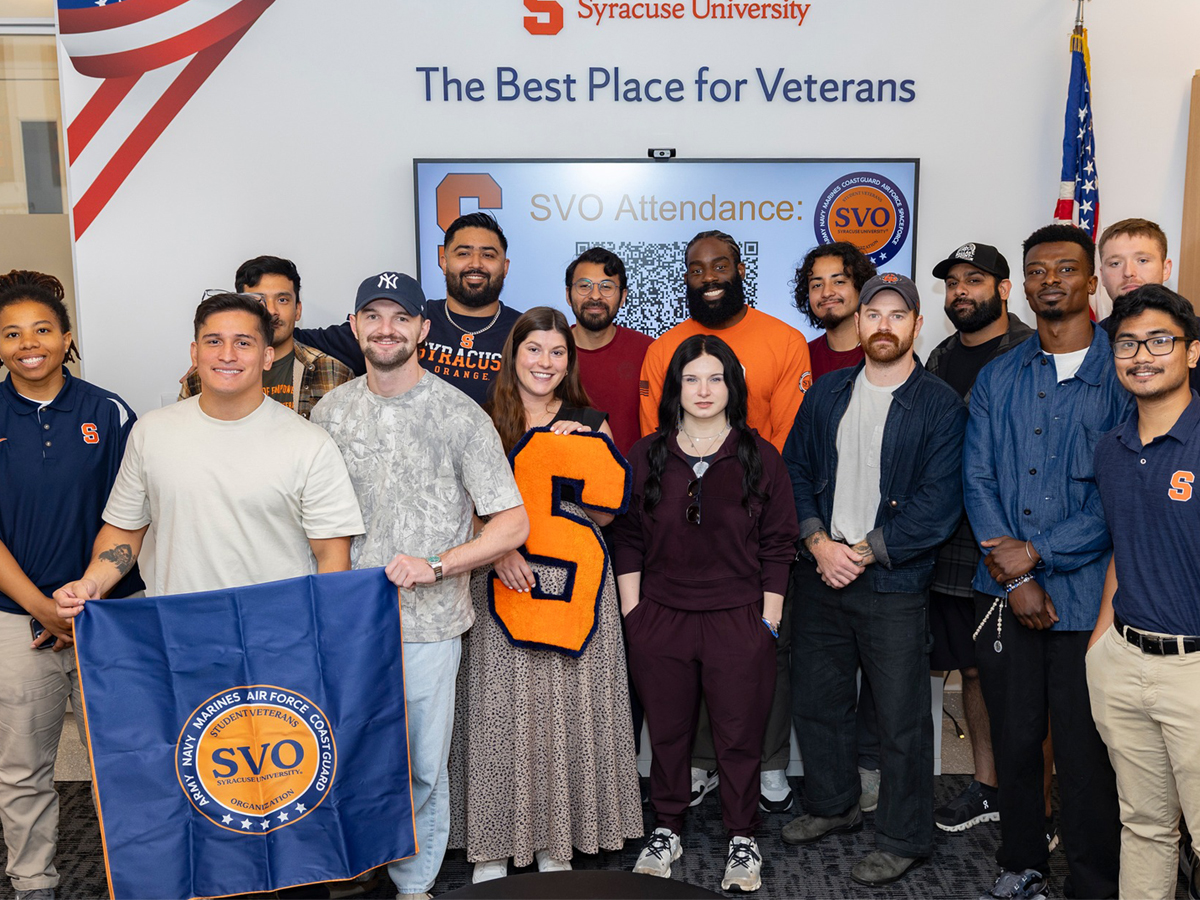 Syracuse University student veterans gather for a group photo holding an SVO flag and large orange "S" beneath a banner reading "The Best Place for Veterans."