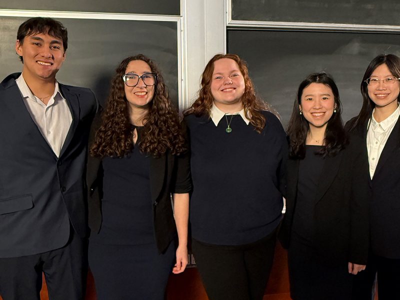 Group picture of five students, four women and one man, all wearing black and smiling