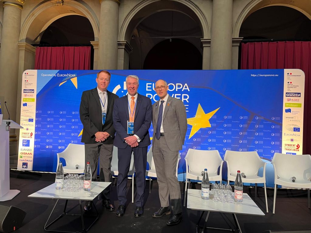 Three men in suits with a blue background behind them,