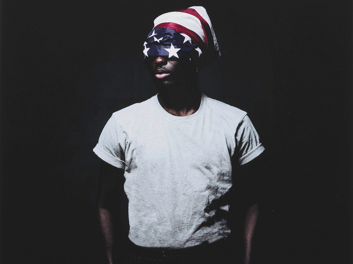 Portrait of a Black Man with an American flag partially covering his face.