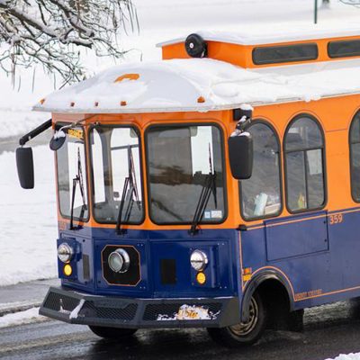 A campus trolley drives along a snow-covered road.