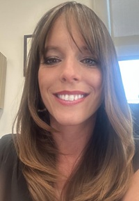 A person smiles while posing for a headshot indoors.