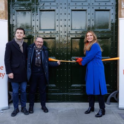 Three people stand in front of large green doors, cutting an orange ribbon between two Syracuse University Florence banners.