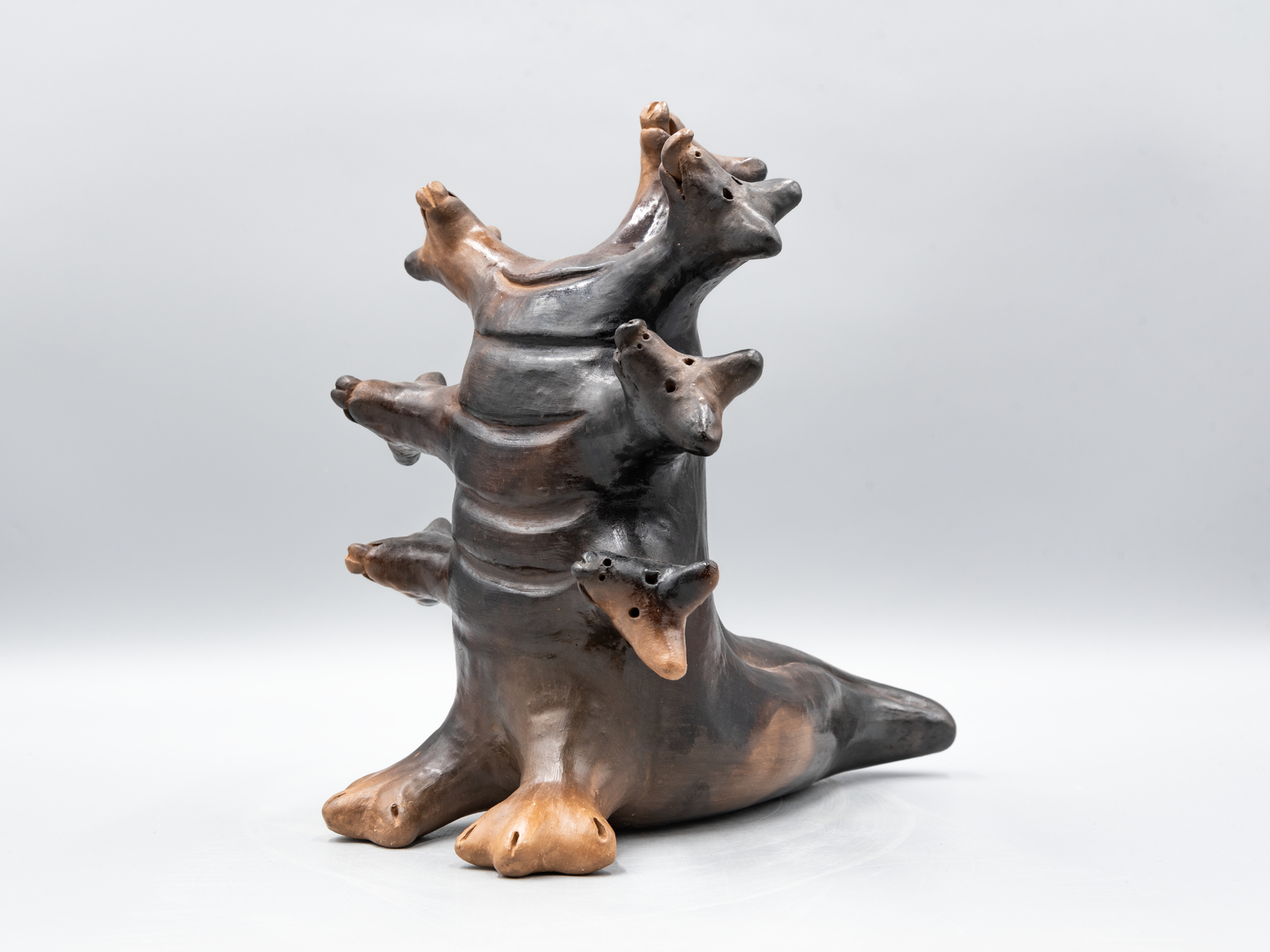 Pit-fired ceramic sculpture of seven-headed mythological creature in gray and brown tones.