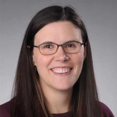 A person smiles while posing for a headshot in front of a grey backdrop.