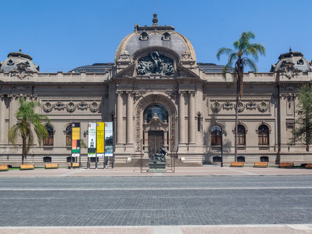 The facade of the Museo Nacional de Bellas Artes with decorative sculptures, arched entrance, and palm trees flanking the building in Santiago, Chile.