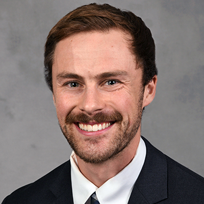 A medical student smiles while posing in front of a grey backdrop.