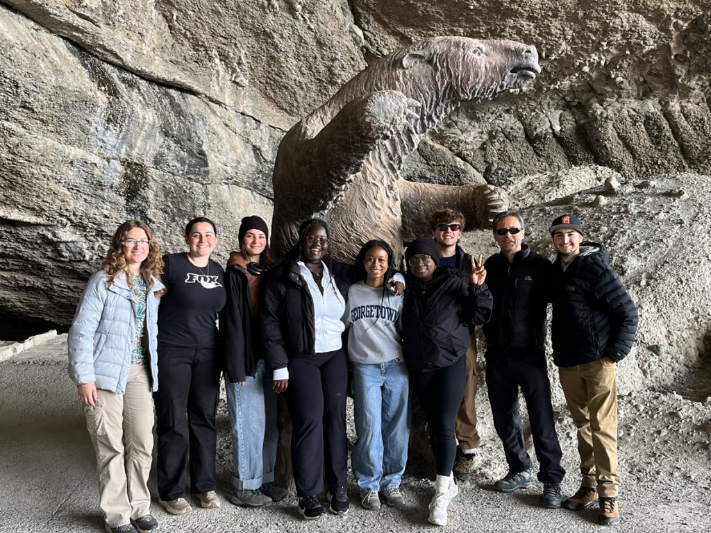 Group of Syracuse University students and faculty posing in front of a large fossil carved into a cave wall in Chile.