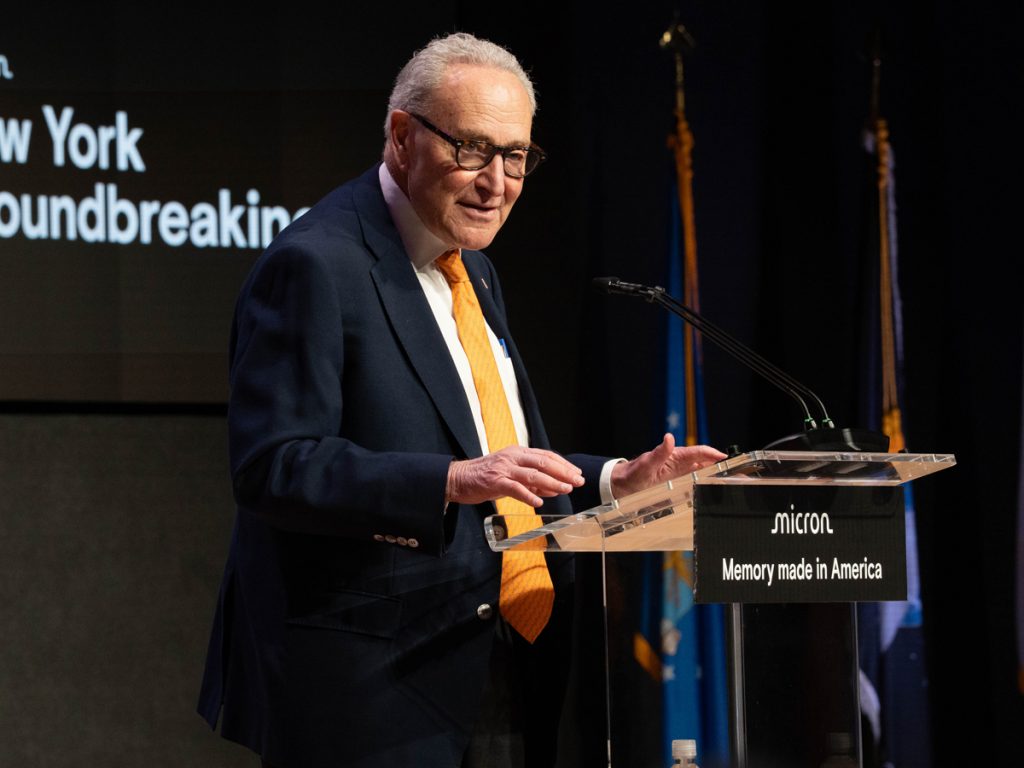 A person speaks to a crowd while standing in front of a podium.