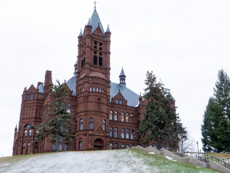 Historic red‑brick academic building with a clock tower on a snowy hillside