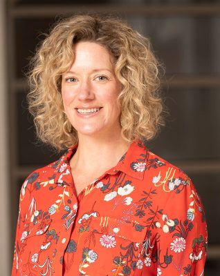 A person smiles while posing for a headshot indoors.