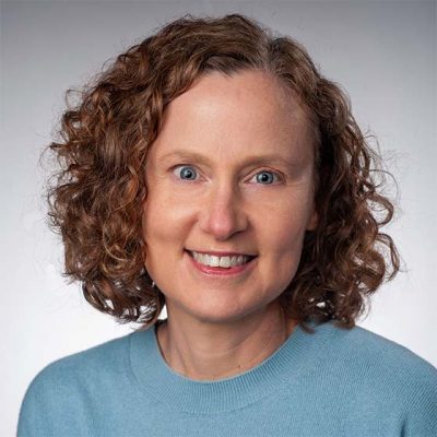 A professor smiles for a headshot in front of a grey backdrop.