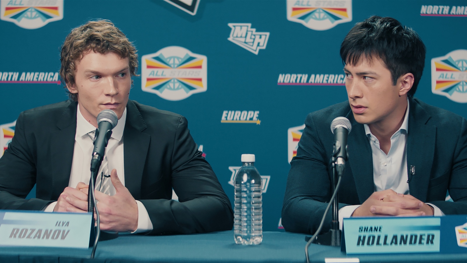 wo hockey players sit at a press conference table with microphones and nameplates in front of a branded All‑Star event backdrop.