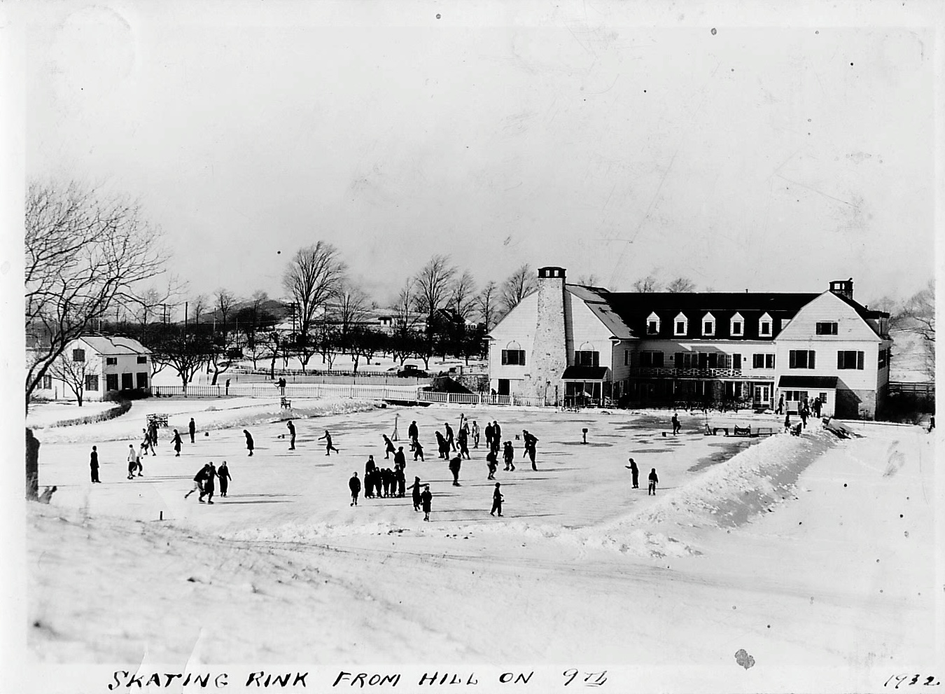 People skating on an outdoor ice rink in front of a large lodge-style building in winter.