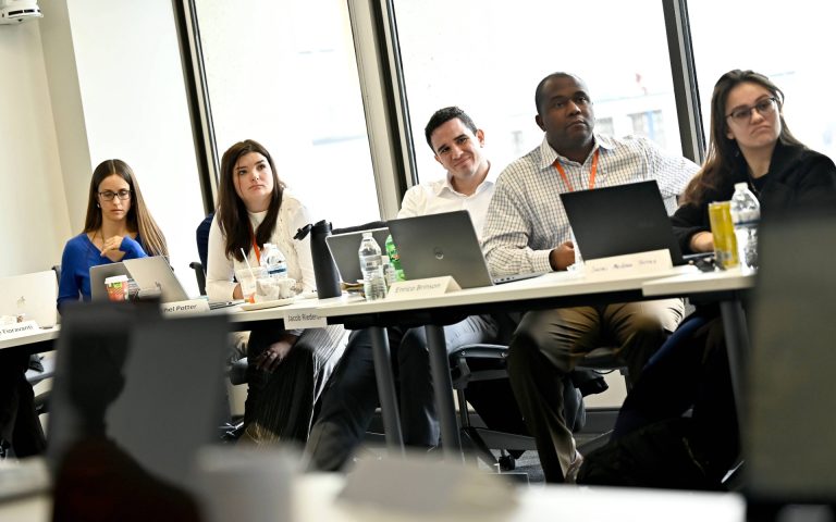 People sitting near large windows at a meeting table, working on laptops and taking notes.