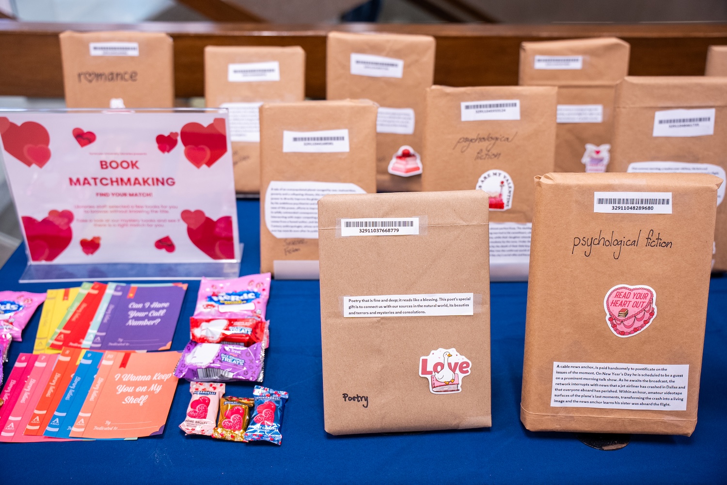 A display of brown paper wrapped books with handwritten and typed descriptions alongside colorful valentines and candies