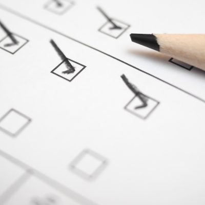 A pencil resting on a checklist with several boxes marked with checkmarks.