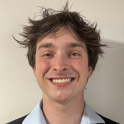 A student smiles while posing for a headshot in front of a white wall.