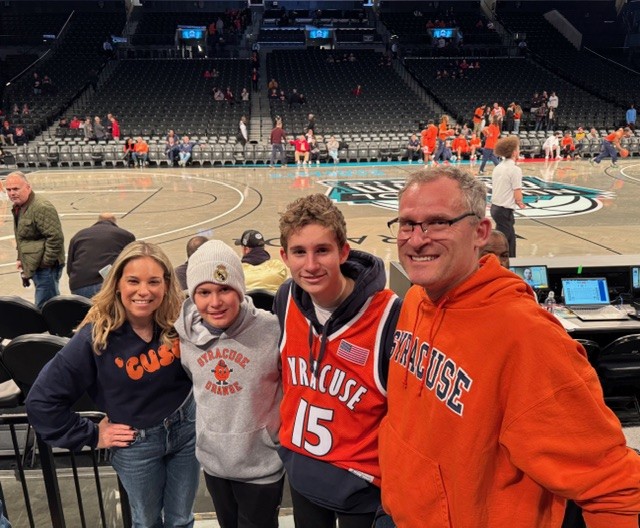 Group of people wearing Syracuse apparel posing courtside at a basketball arena