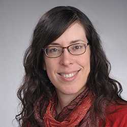 Woman with red top, long brown hair, glasses, smiling