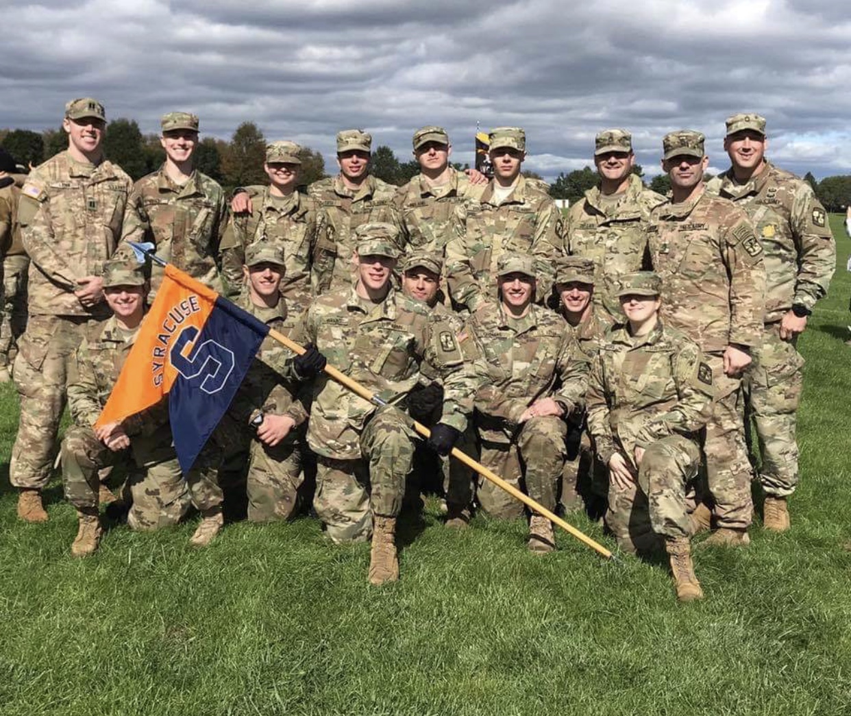 Men and women in military camouflage with a Syracuse flag.
