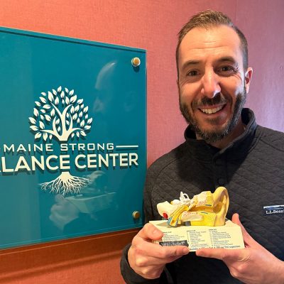 Man standing with an inner ear model and a sign that says Maine Strong Balance Center