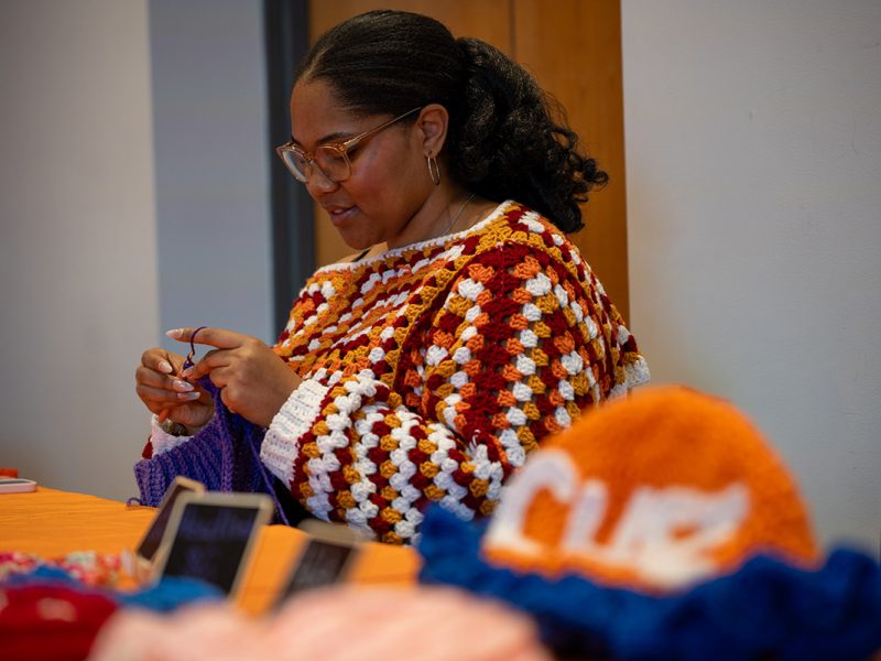 Individual crochets a colorful blanket with other knitted items displayed on a table