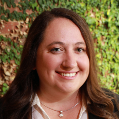 A person smiles while posing for a headshot in front of an ivy covered wall.