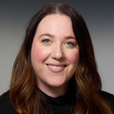 A person smiles while posing for a headshot in front of a grey backdrop.