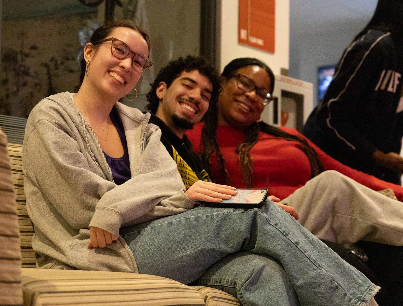Three people sitting on a couch in a lounge area, smiling warmly at the camera