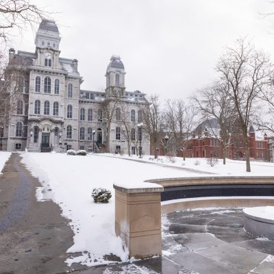 Snow-covered campus with a large historic building in the background and a circular memorial area in the foreground.