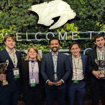 Members of the University's sport analytics team, four men and one woman, stand with the awards they won.