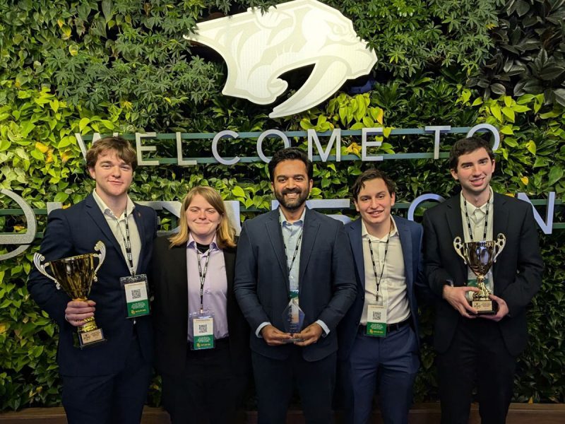 Members of the University's sport analytics team, four men and one woman, stand with the awards they won.