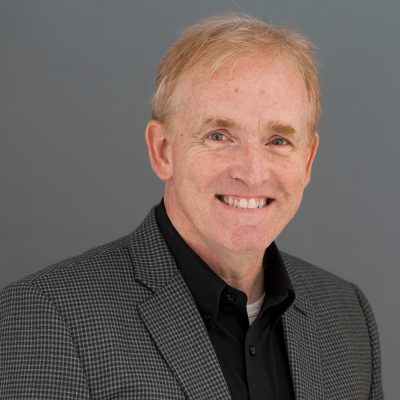 Man in black shirt and grey jacket, smiling